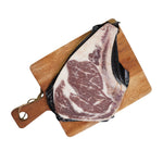 Load image into Gallery viewer, Marbled raw steak on a wooden cutting board with black plastic wrap.
